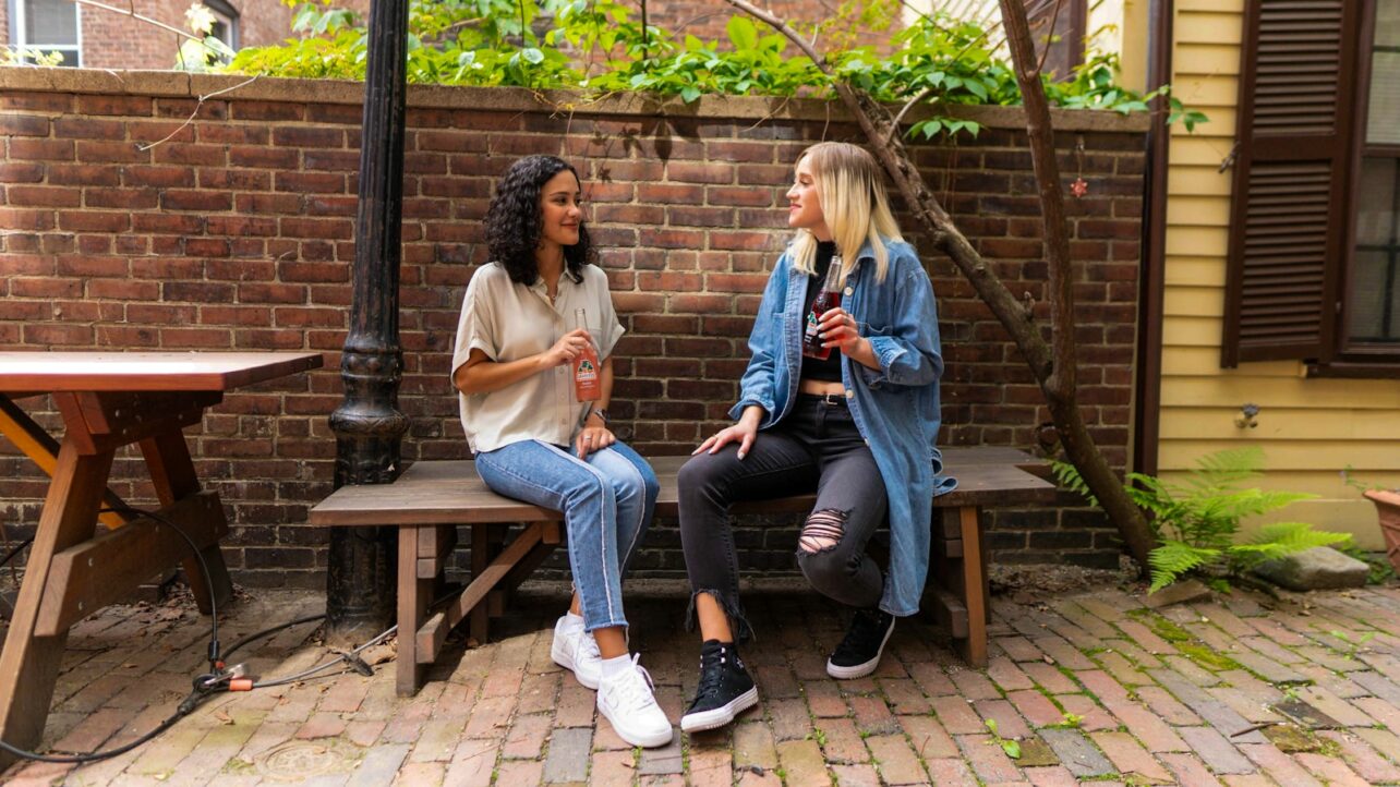 2 women sitting on brown wooden bench